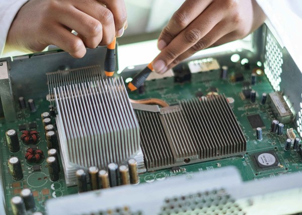 A close-up of hands using a screwdriver to adjust components on a computer's circuit board, with heat sinks and electronic parts visible.