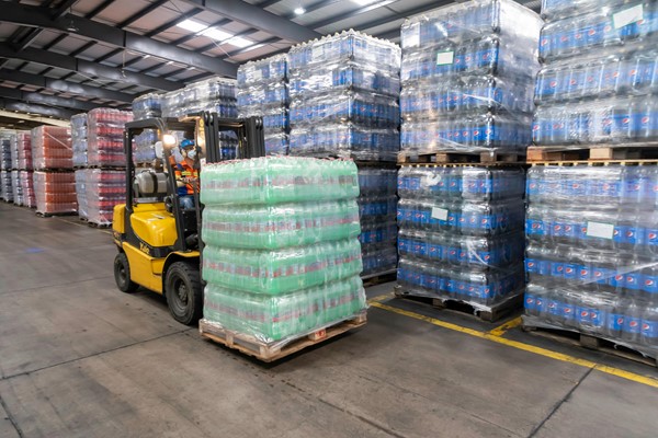 A worker operating a forklift in a warehouse to move a pallet of bottled drinks.