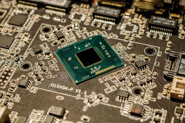 A close-up of a computer circuit board featuring a green microchip at the center surrounded by various electronic components.