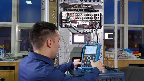  a technician using a power quality analyzer to check signals in a network setup, with various equipment and cables in the background