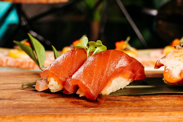 Two pieces of tuna nigiri sushi on a wooden board, topped with small sprouts and presented on a green leaf.