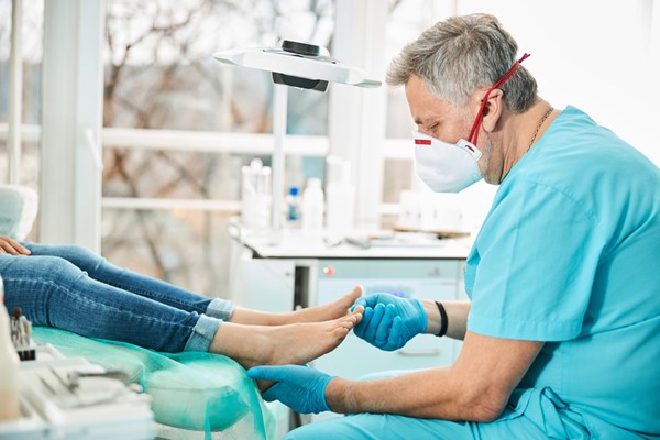 Medical professional examining a patient's foot while wearing a face mask.